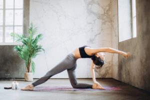Frau in grauen Leggings und schwarzem Sport-BH beim Yoga auf der Yogamatte